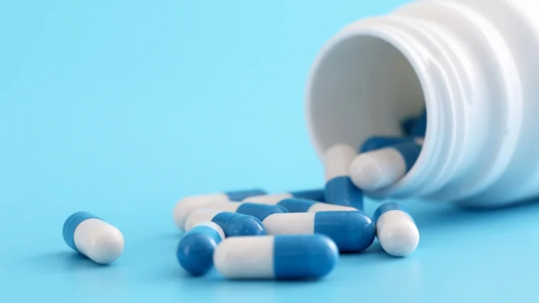 An open bottle of supplements, with blue and while capsules spilling out.
