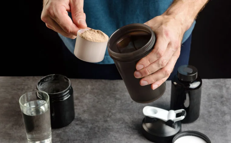 A person scooping out a protein powder into a container.