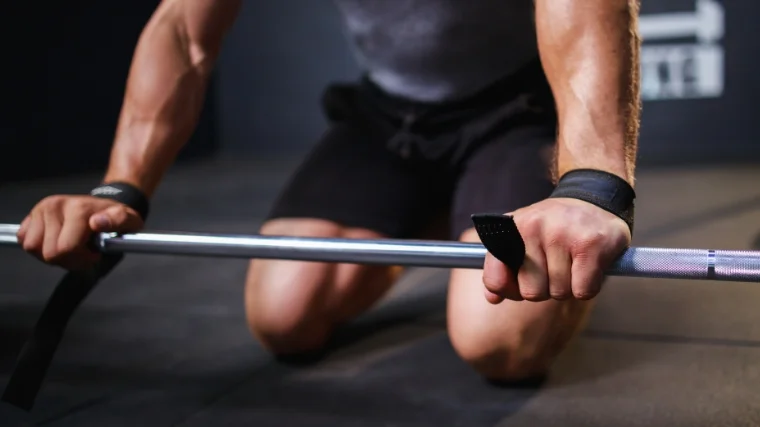 A person using lifting straps with a barbell.