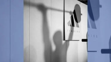 The shadow of a person lifting a barbell is cast across an adidas logo titled "training".