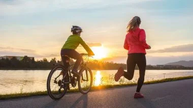 A young person riding a bicycle and a fit adult jogging on a sunny day.