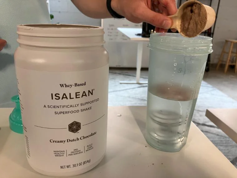 Our tester dumping a scoop of Isagenix IsaLean Shake in their shaker cup.