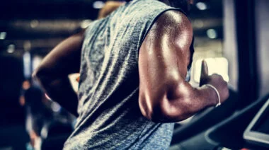 A close up of a person's arm and torso shows them sweating while running on a treadmill.