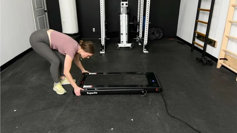 A woman in a gym reaches down grabbing the handle bar on a SuperFit Treadmill