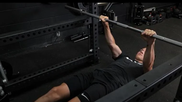 A person performing the barbell inverted row exercise.
