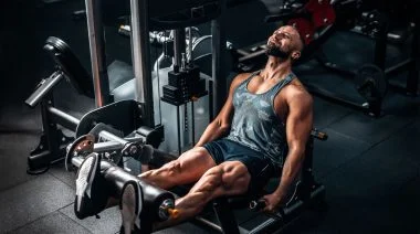 A muscular person doing leg extension exercise on the machine